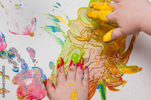 The hand of the child paints with paints on a paper