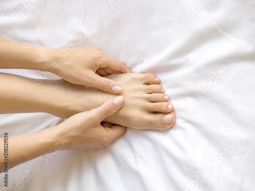 Young woman massaging her foot on the bed. Healthcare concept.