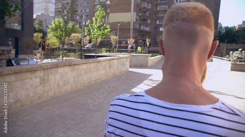 caucasian man with fair hair using smartphone outdoors. casual male sharing photos in social media walking past buildings sunny day