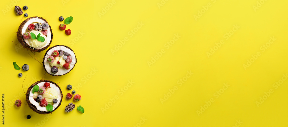 Coconut ice cream with fresh berries in coconuts halves on yellow