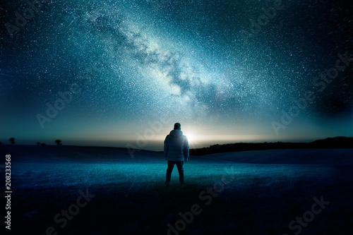 A man stands watching with wonder and amazement as the moon and milky way galaxy fill the night sky. Night time landscape. Photo composite. photo