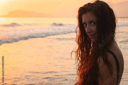 Close up portrait of attractive young woman on the beach. In the background sea and sunset. © jonnyslav