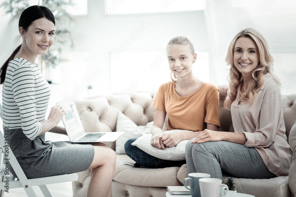 Family issue. Joyful female psychologist using laptop while positive mother and daughter smiling to camera Family issue. Joyful female psychologist using laptop while positive mother and daughter smiling to camera