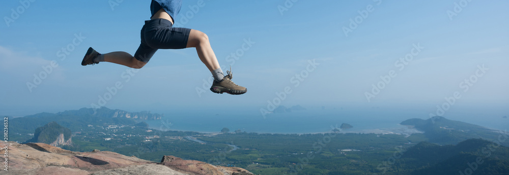 Young woman jumping on mountain peak cliff edge