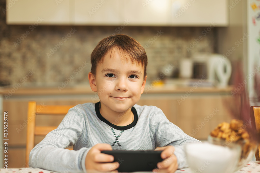 Little boy sitting at table holding a phone in his hands Little boy sitting at table holding a phone in his hands