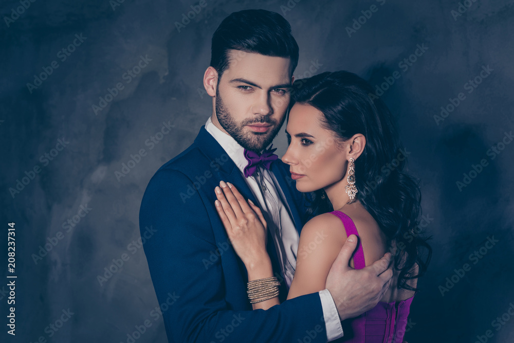 Portrait of pretty charming mrs in purple dress with jewelry half face mr in tuxedo bowtie holding hand in pocket of pants embracing his lover lovely attractive couple isolated on grey background - obrazy, fototapety, plakaty 