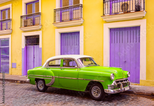 Green and White Vintage Car in Cuba Parked in Front of a Yellow and Purple Building © lindahughes