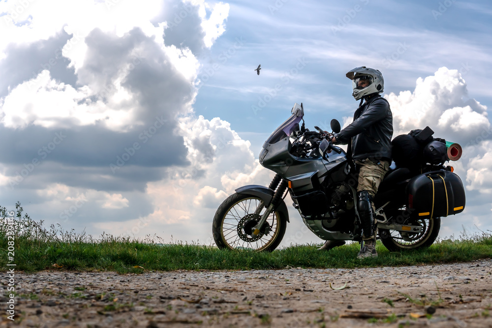 Rider Man and off road adventure motorcycles with side bags and equipment for long road trip, river and clouds on background, enduro travel touring concept