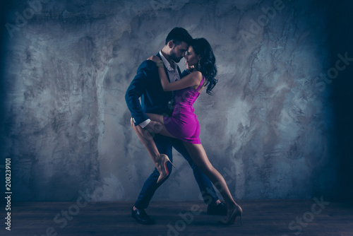 Full size fullbody portrait of romantic lovely couple, pretty lady in purple tight dress gentlemen in tuxedo, face to face standing close in tango position, isolated on concrete background