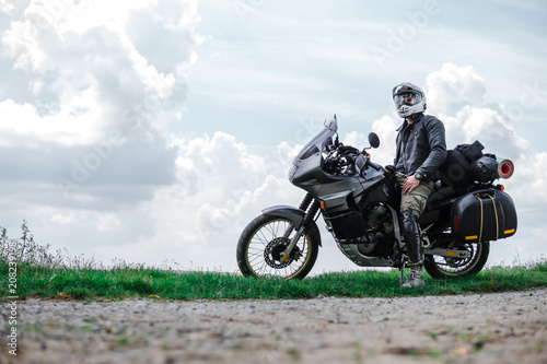 Rider Man and off road adventure motorcycles with side bags and equipment for long road trip  river and clouds on background  enduro travel touring concept