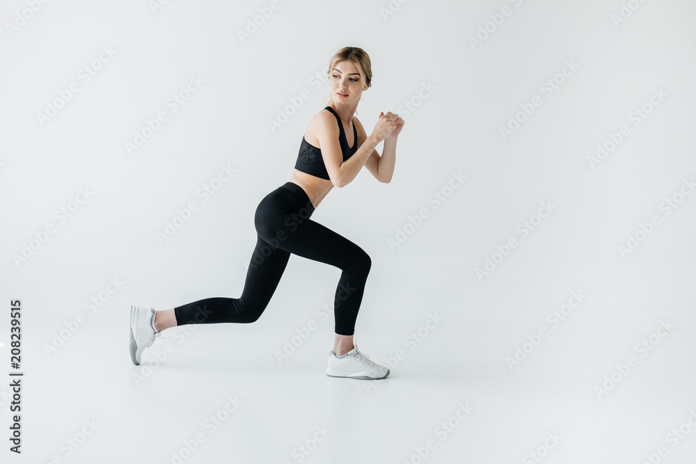 Side view of young athletic sportswoman doing lunges isolated on grey