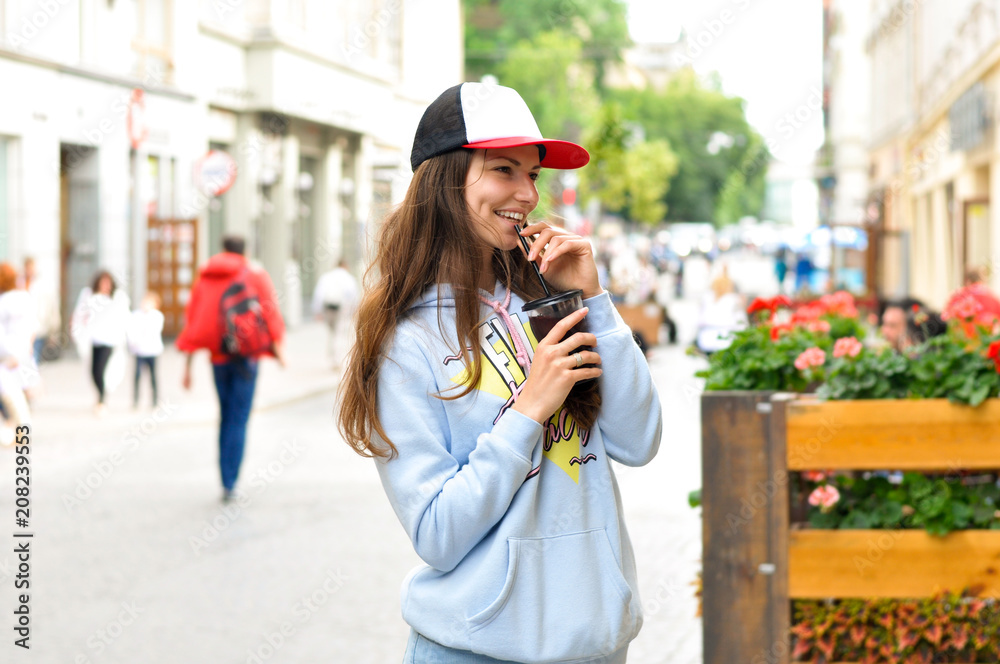 young woman tourist walking around the city and drinking a cold cocktail in hip hop style clothes