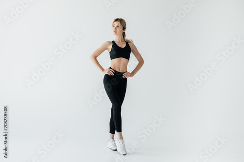 beautiful sportswoman akimbo in black sportswear standing isolated on grey