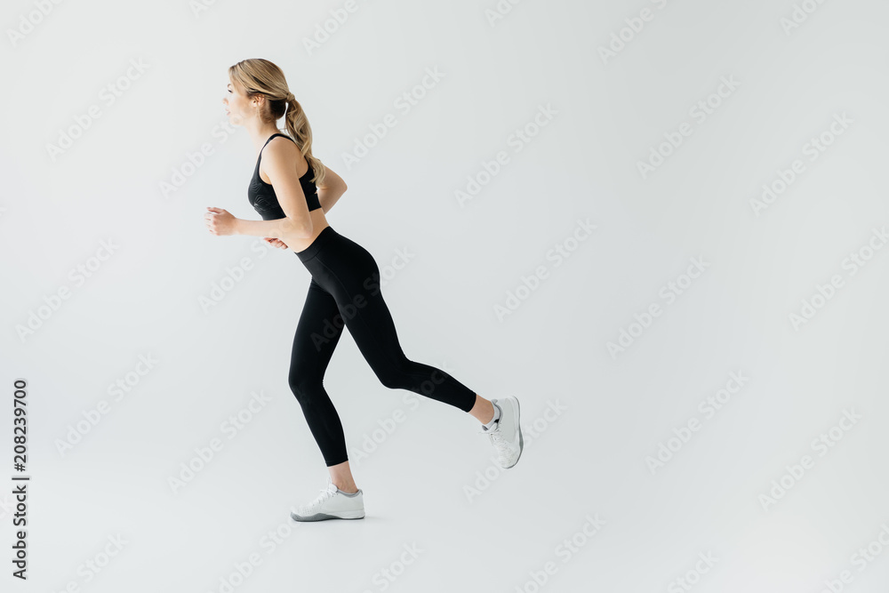 Side view of young athletic sportswoman running isolated on grey Side view of young athletic sportswoman running isolated on grey