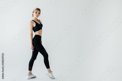 side view of young blond sportswoman in black sportswear posing isolated on grey
