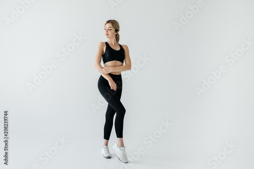young blond sportswoman in black sportswear posing isolated on grey