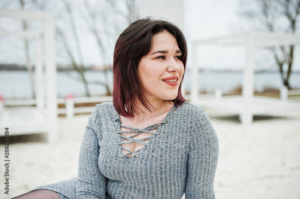 Portrait of brunette girl in gray dress sitting at white wooden construction. Portrait of brunette girl in gray dress sitting at white wooden construction.