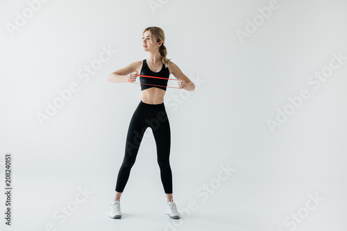 young athletic woman exercising with rubber tape isolated on grey