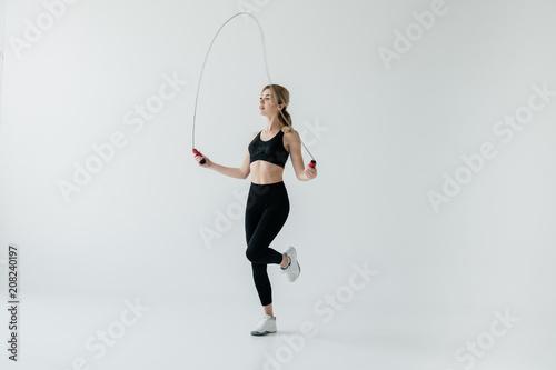 young sportive woman exercising with skipping rope isolated on grey photo