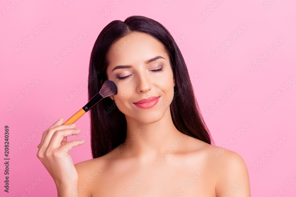 Sensual charming pretty woman applying blusher on her cheekbones using make-up brush with close eyes isolated over pink background Sensual charming pretty woman applying blusher on her cheekbones using make-up brush with close eyes isolated over pink background