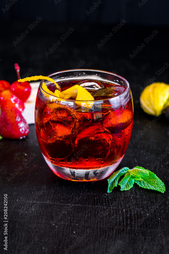 Red cocktail with ice and orange on black background