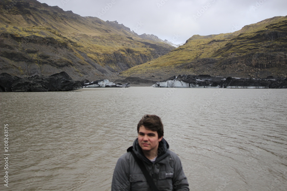 Young male tourist posing in front of mountains and icebergs in the background, photo taken in Iceland