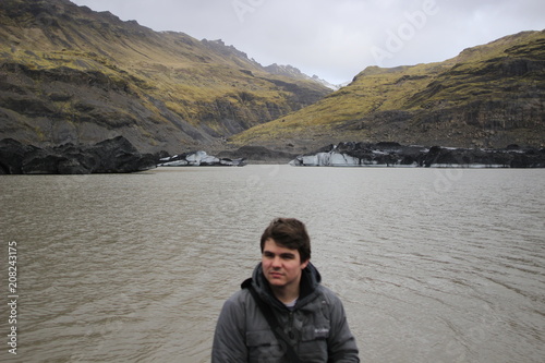 Young male tourist posing in front of mountains and icebergs in the background, photo taken in Iceland © mynewturtle