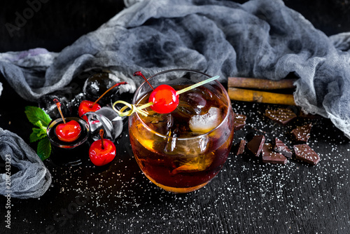 Glass of whiskey with ice and cherry on black background
