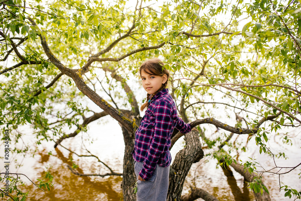 Serious girl with pigtails is standing on a tree branch Serious girl with pigtails is standing on a tree branch