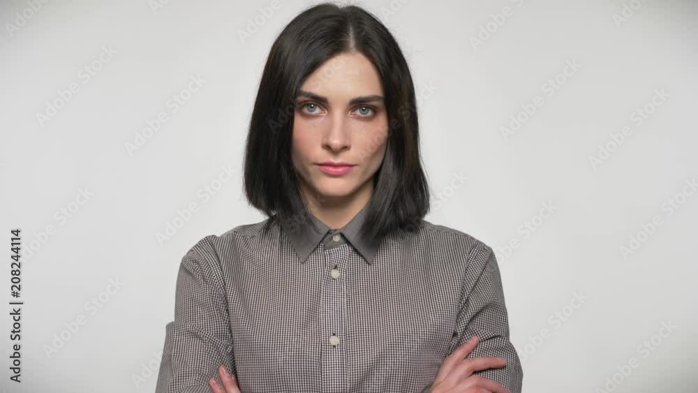 Young beautiful woman standing with crossed hands and looking in camera, confident and serious, white background Young beautiful woman standing with crossed hands and looking in camera, confident and serious, white background