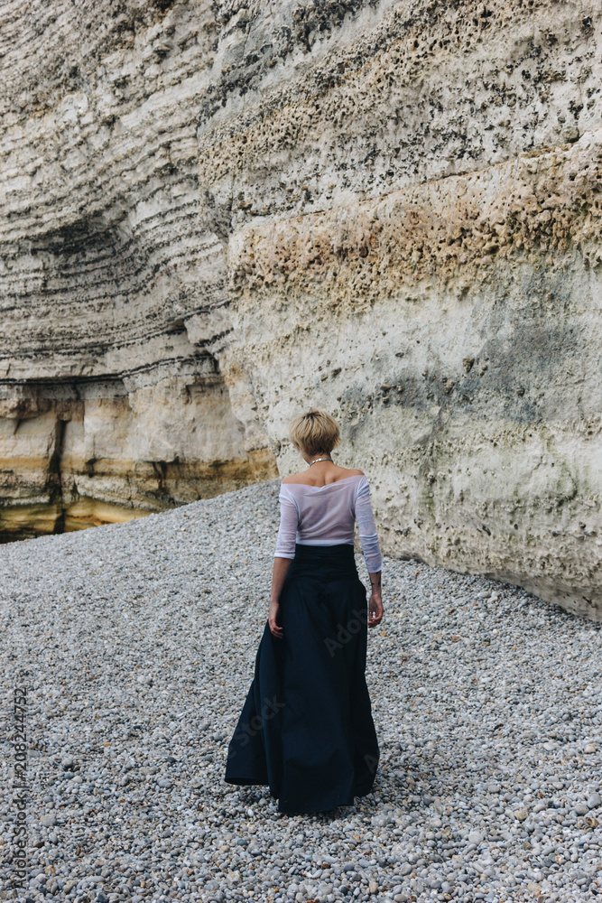 rear view of elegant girl walking on shore near cliff, Etretat, Normandy, France