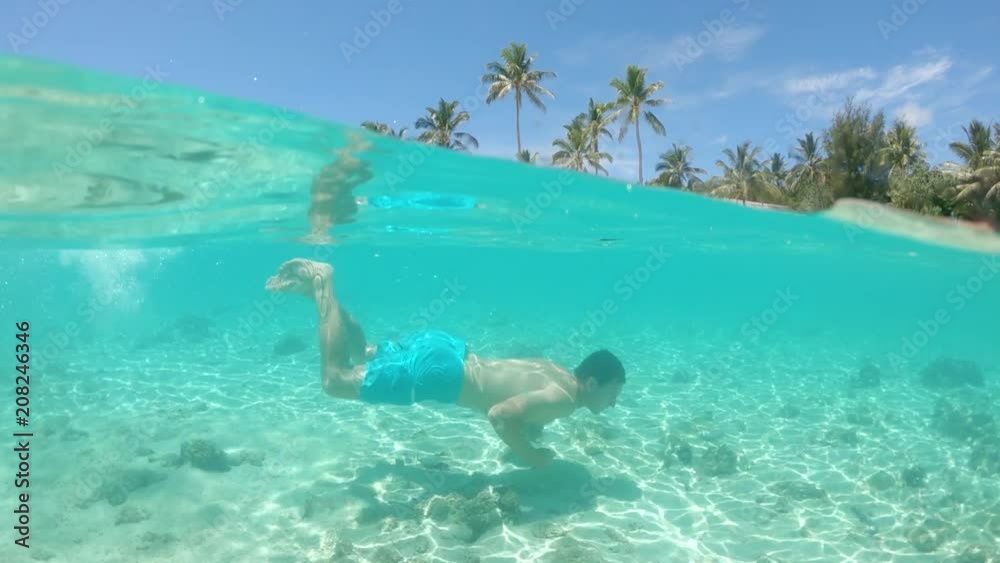 SLOW MOTION, HALF UNDERWATER: Young man swimming along the white sand beach of picturesque tropical island. Cheerful male cools off by diving in tranquil glassy ocean. Awesome summer holiday activity. SLOW MOTION, HALF UNDERWATER: Young man swimming along the white sand beach of picturesque tropical island. Cheerful male cools off by diving in tranquil glassy ocean. Awesome summer holiday activity.