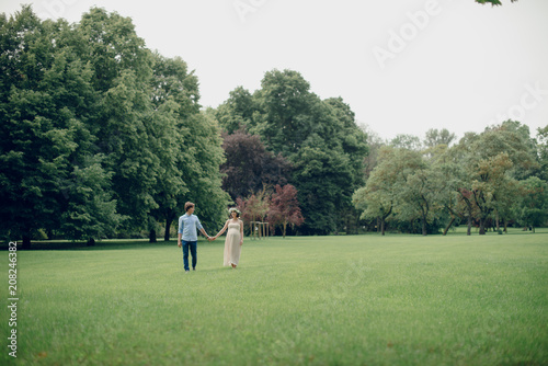 Happy young family walking in the meadow in the park. Pregnant woman and her husband holding hands. Summer day. Couple of man and woman © WellStock