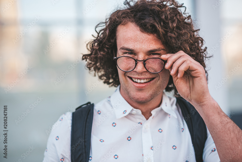 Horizonrtal close up portrait of happy smiling handsome male with curly hair, looks from trendy spectacles surprisely aside, notices something good on the street. People, lifestyle, business concept Horizonrtal close up portrait of happy smiling handsome male with curly hair, looks from trendy spectacles surprisely aside, notices something good on the street. People, lifestyle, business concept