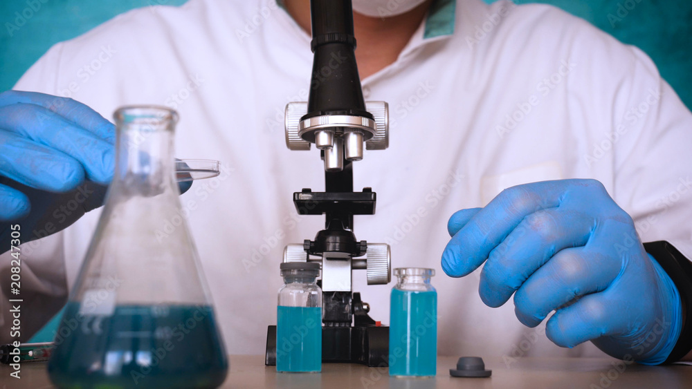 The alchemist, a biologist, takes the DNA of various substances, in a respirator, in a protective cap, in goggles, in a white medical gown, a flask, a green background, a science table. The alchemist, a biologist, takes the DNA of various substances, in a respirator, in a protective cap, in goggles, in a white medical gown, a flask, a green background, a science table.