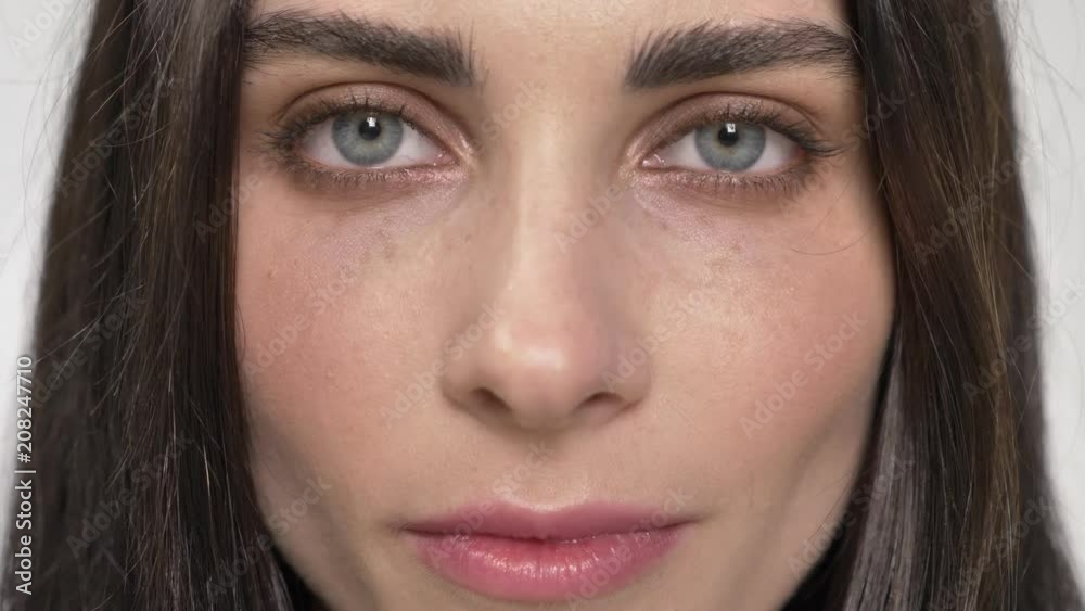 Portrait of young pretty woman with blue eyes looking straight into camera and blinking, closing eyes, white background Portrait of young pretty woman with blue eyes looking straight into camera and blinking, closing eyes, white background