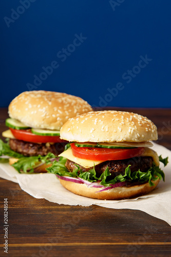 Classical burger with beef patty, tomatoes, cheese, onion, cucumber and lettuce served on wooden table against blue background