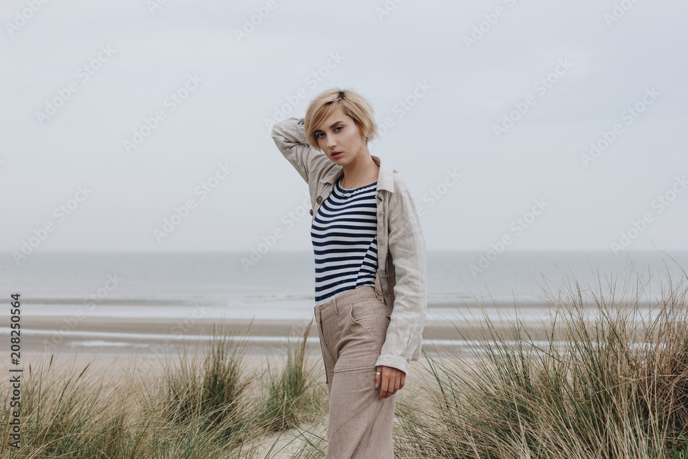 stylish young woman in striped shirt and jacket on sandy shore