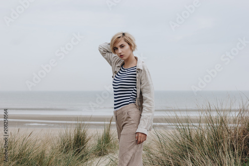 stylish young woman in striped shirt and jacket on sandy shore