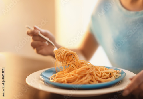 Young woman eating tasty pasta at table, closeup