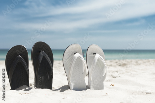 Two pair of white and blackn flip-flops in the sand. Summer vacation concept