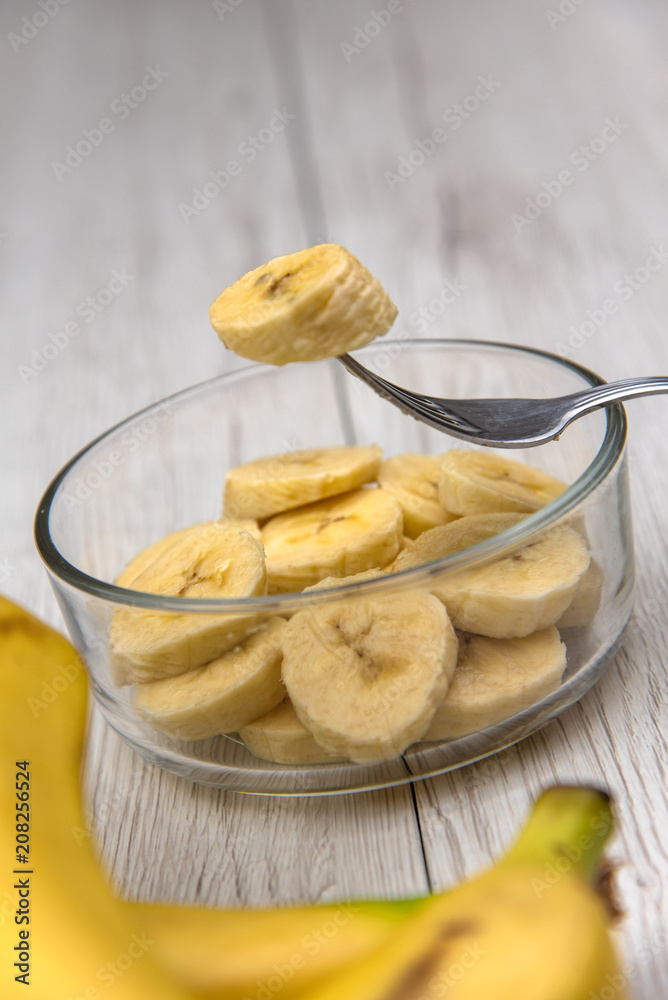 Raw yellow banana fruit slices in a bowl whit a fork on white wood table Raw yellow banana fruit slices in a bowl whit a fork on white wood table