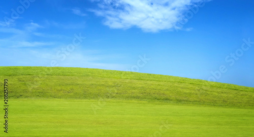 Panoramic view of green grass field with hill on blue cloudy sky in background