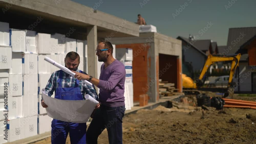 Young man with blueprints talking to construction worker at building site
Young man with blueprints talking to construction worker at building site