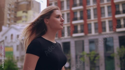 portrait caucasian woman walking in town. girl with blond hair wearing black dress walks along beautiful building
