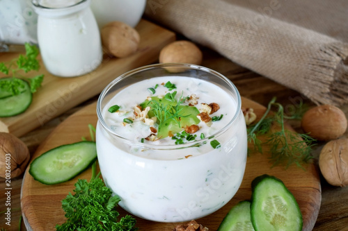 Cold soup with kefir in a glass jar topped with nuts, herbs and cucumber
