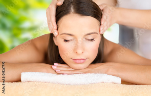 wellness, spa and beauty concept - close up of beautiful woman having face massage over green natural background