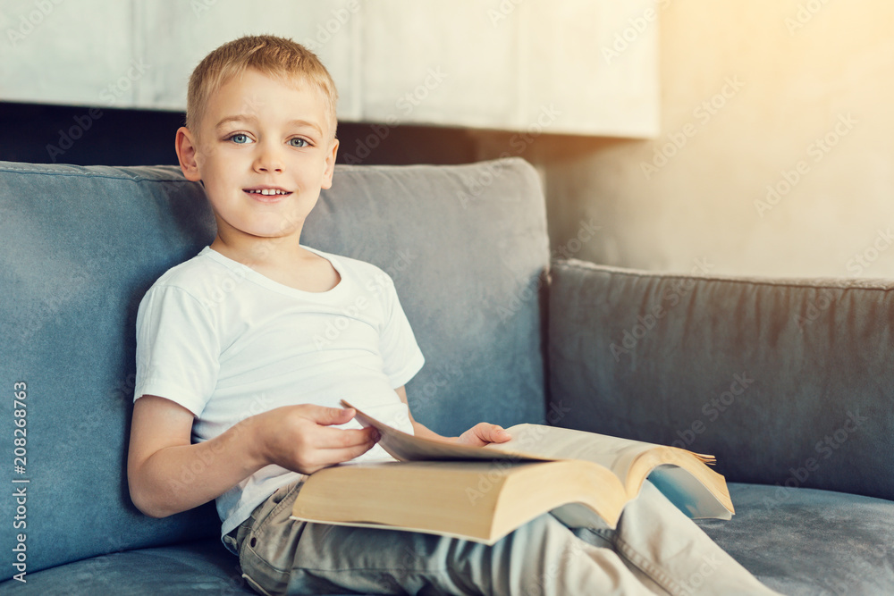 Giant book. Smiling pretty little boy sitting on the sofa and holding a big heavy old book Giant book. Smiling pretty little boy sitting on the sofa and holding a big heavy old book