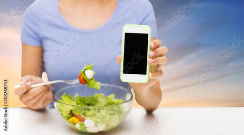 healthy eating, technology, food and people concept - close up of young woman with smartphone and vegetable salad over sky background