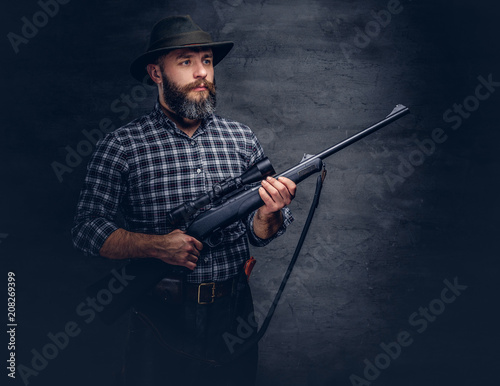 Handsome bearded hunter traveler in a fleece shirt and hat holds rifle with a sight.  © Fxquadro